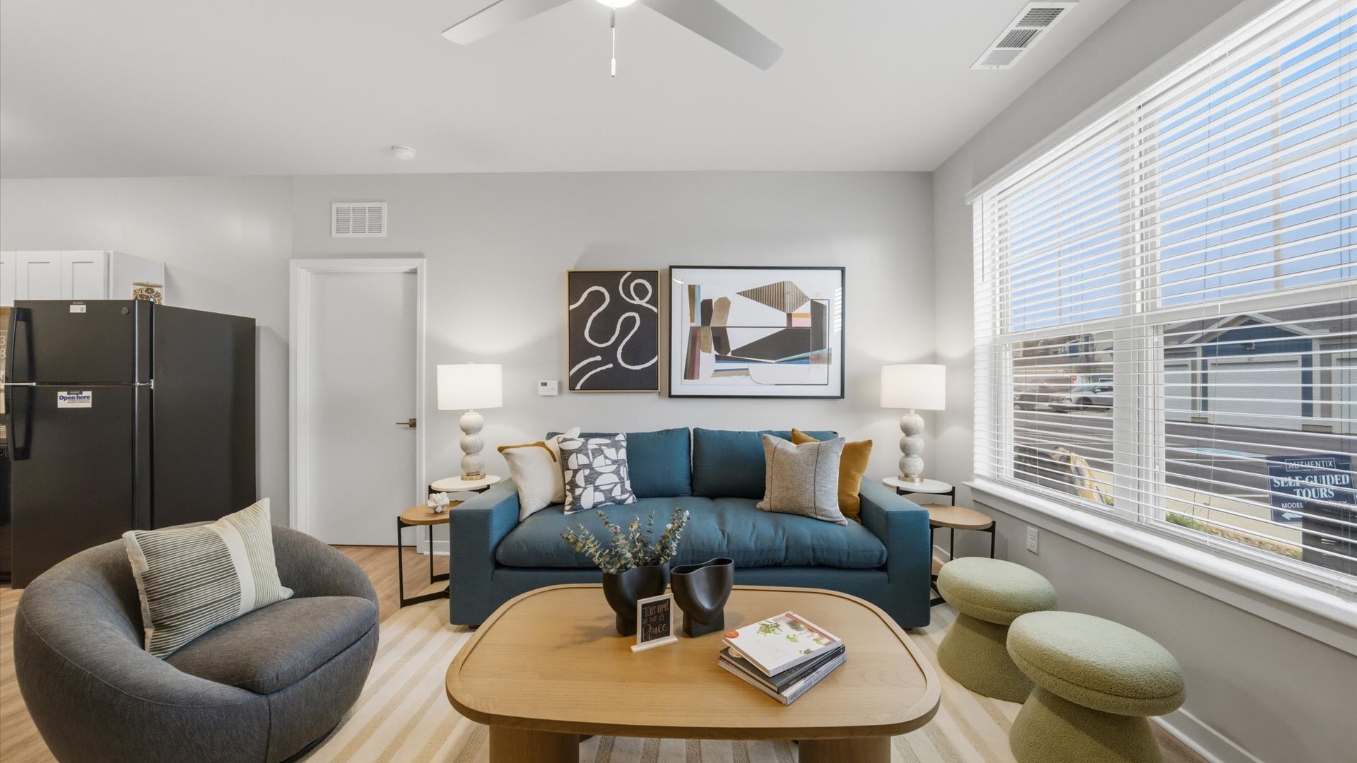 Open living room with blue sofa, wood‑look floors, and abstract wall art in 2 bedroom model home.
