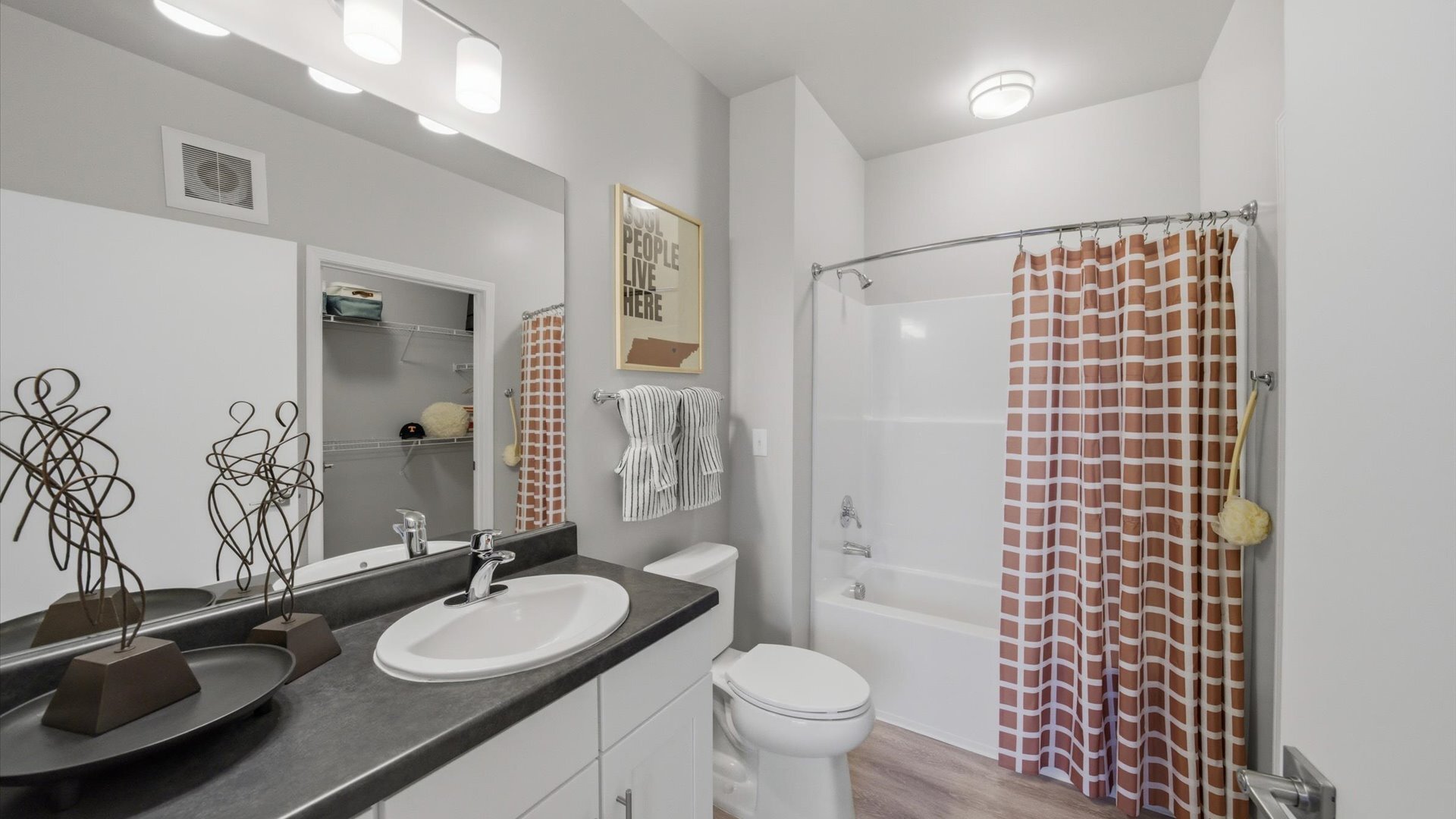 Bathroom with single vanity, dark countertop, and tub/shower combo with patterned curtain at Authentix Town Creek.