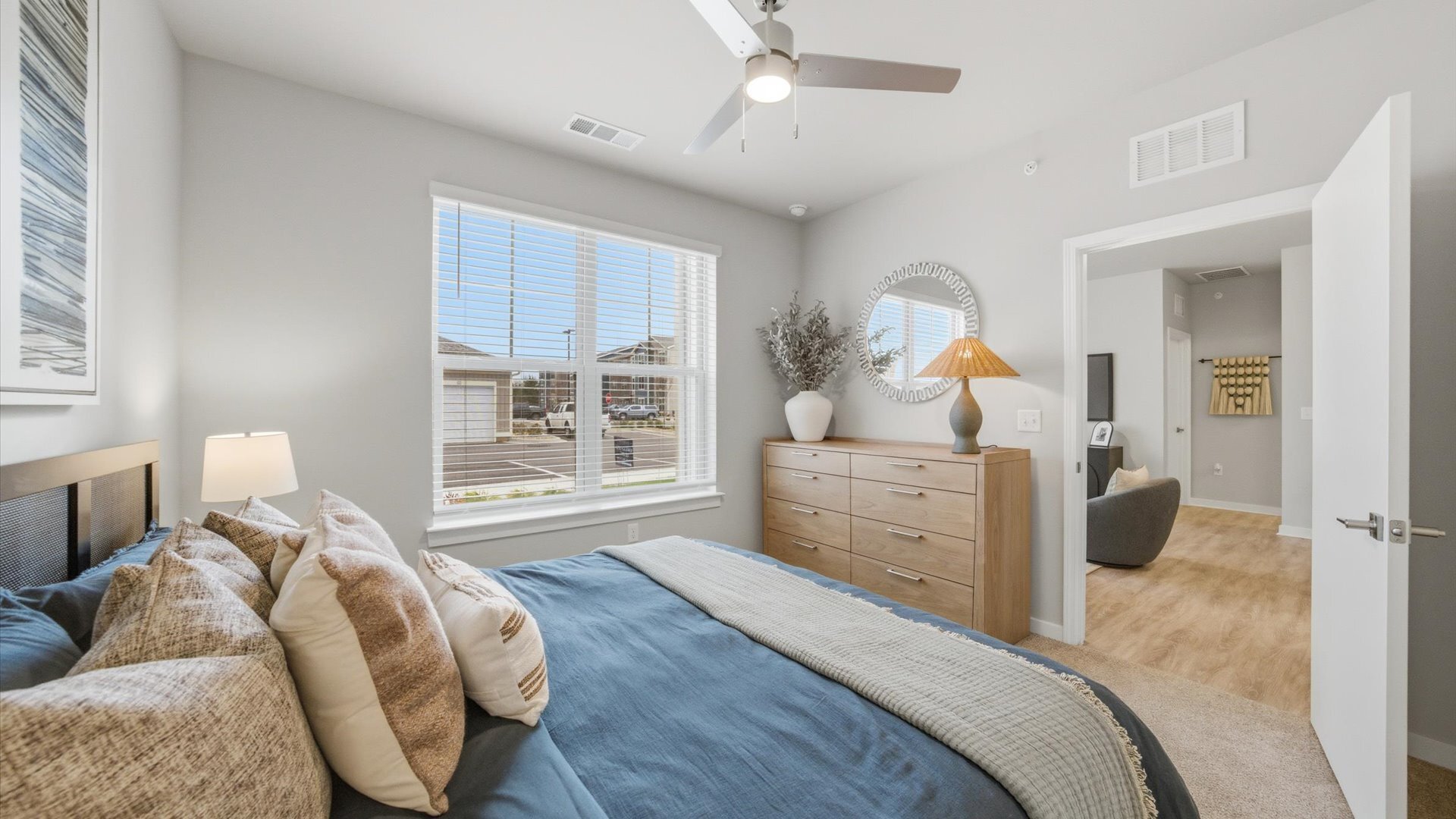 Spacious bedroom with blue comforter, wood dresser, and mirror off of the living room at Authentix Town Creek Apartments.
