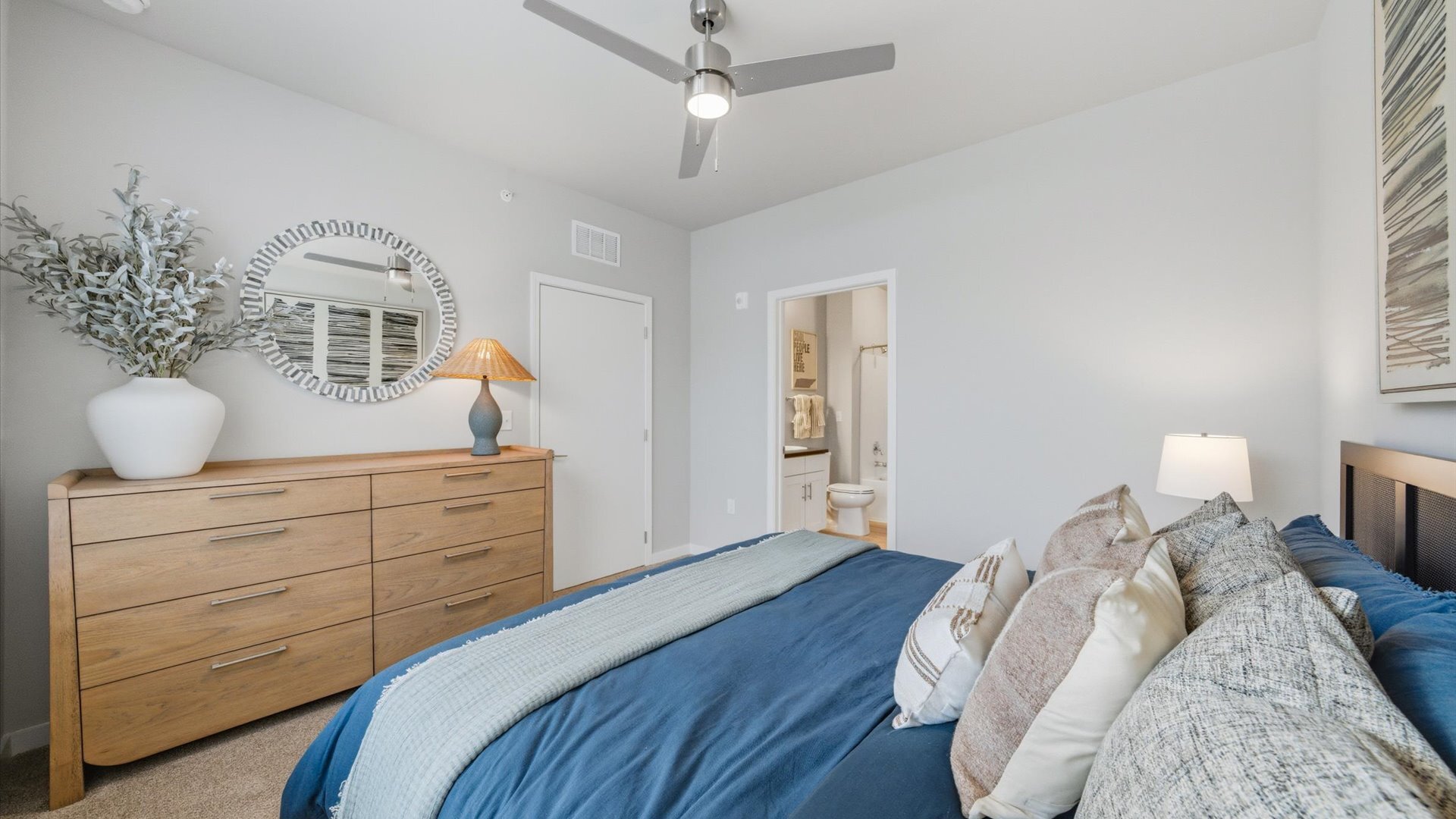 Bedroom with blue comforter, wood dresser, and large window overlooking community at Authentix Town Creek Apartments near Maryville, TN.