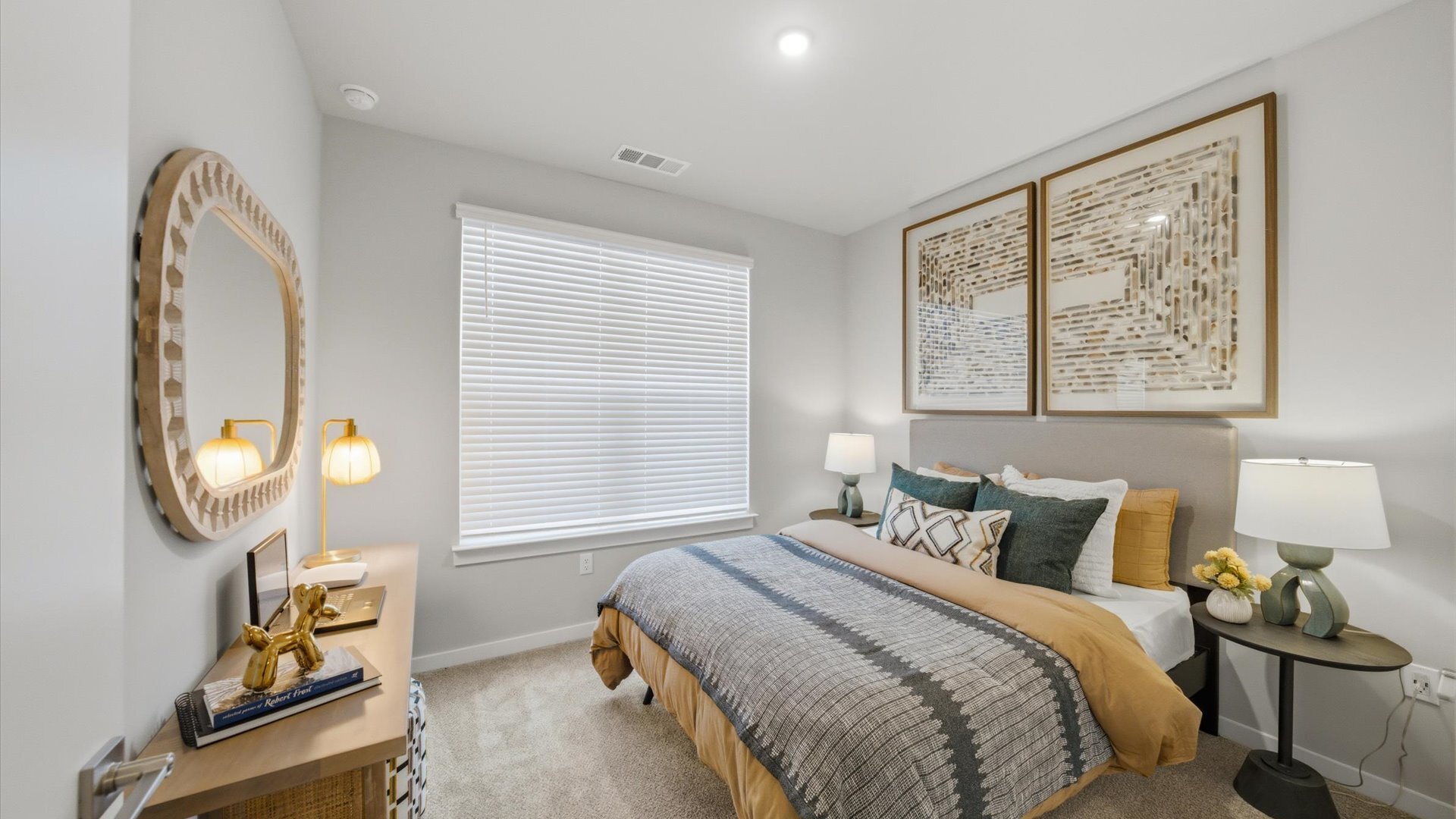 Bright bedroom featuring carpet flooring, decorative mirror, and natural light from wide window in 2 bedroom model home at Authentix Town Creek Apartments.