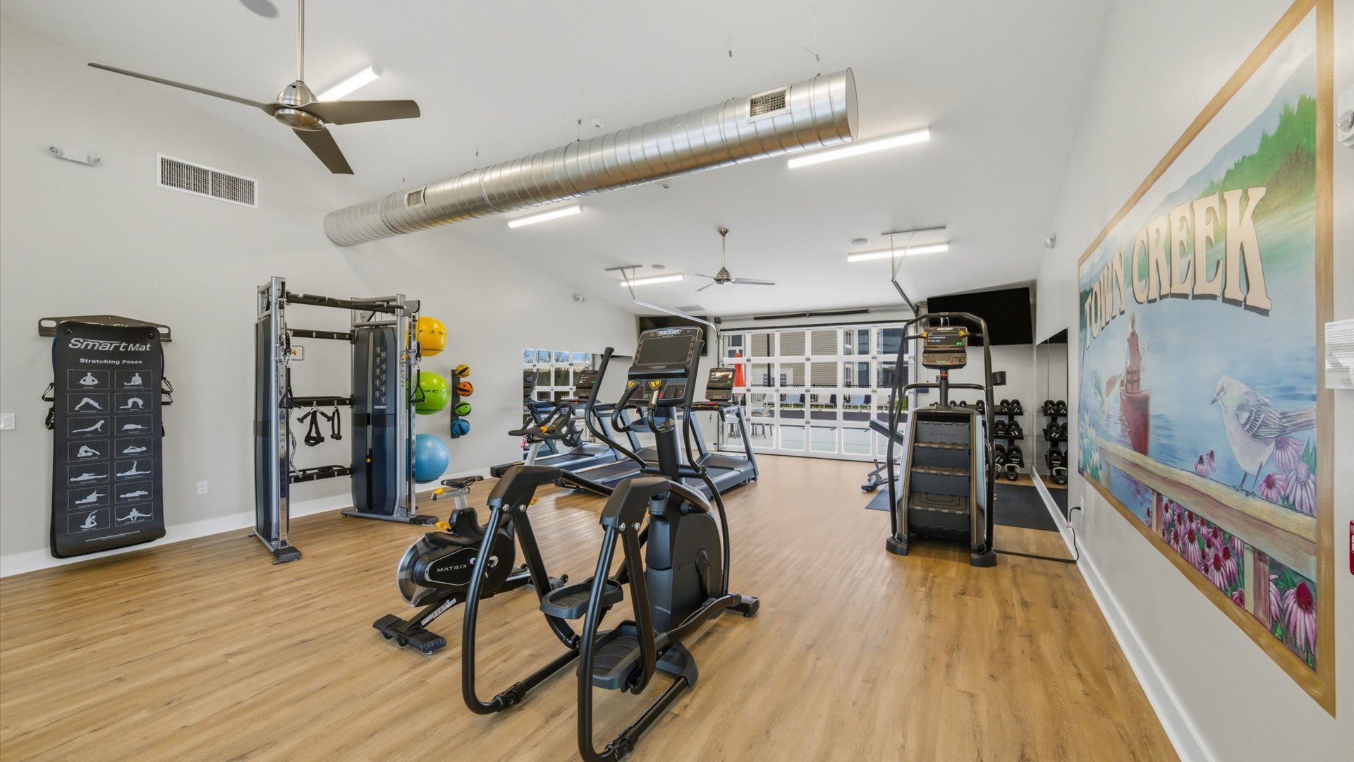 Bright gym with wood‑look floors and garage‑style doors opening to green space in Lenoir City, TN.