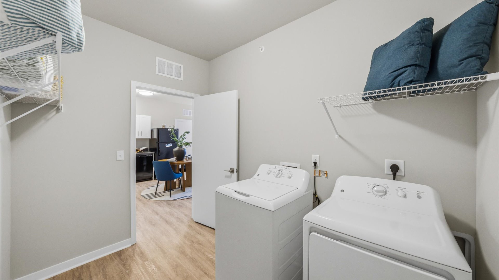 In‑unit laundry room with side‑by‑side washer and dryer plus wire shelving at Authentix Town Creek.