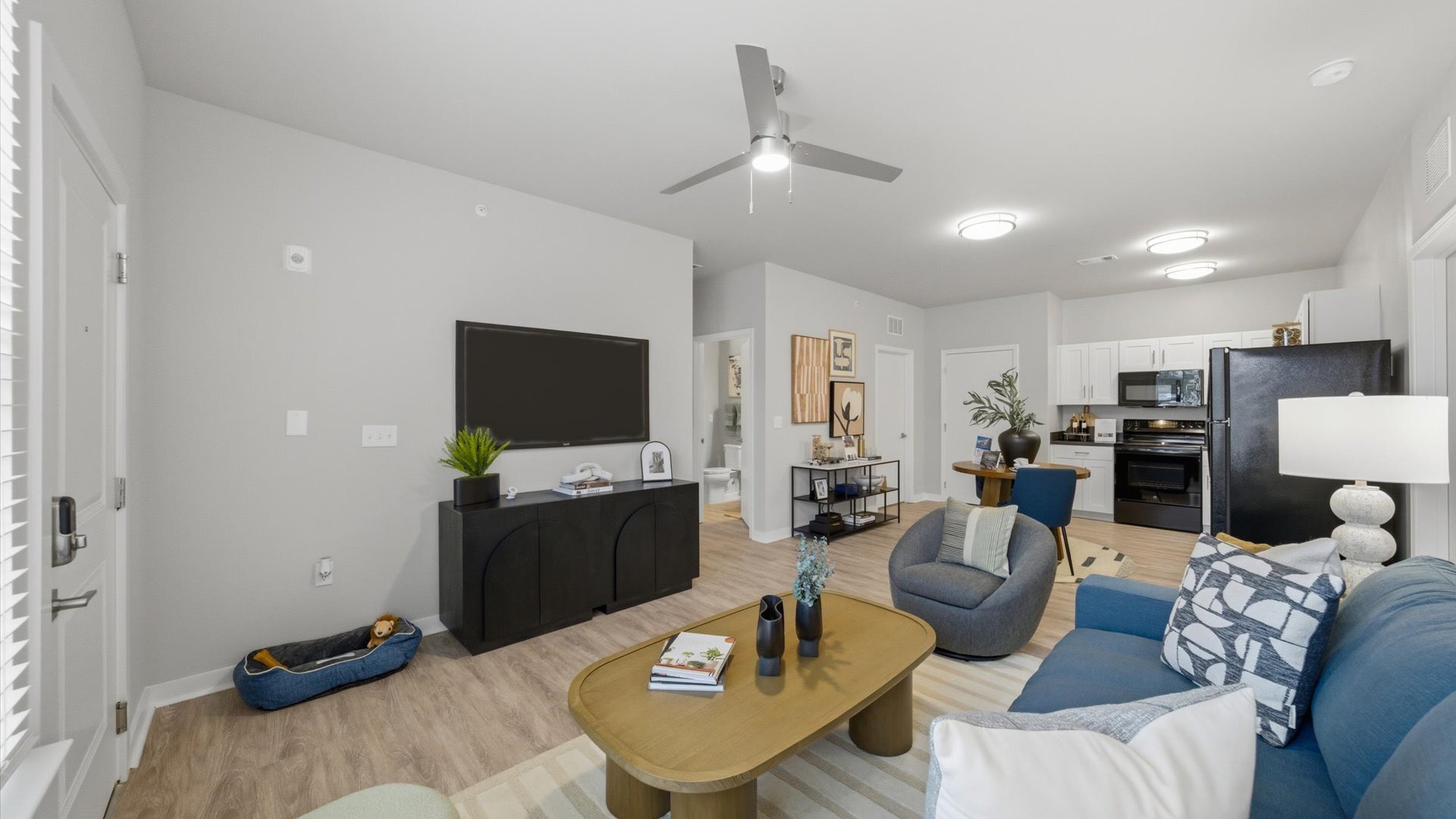 Blue couch, round coffee table, and bright lamps overlooking a modern kitchen with black appliances and white Shaker cabinets at Authentix Town Creek.