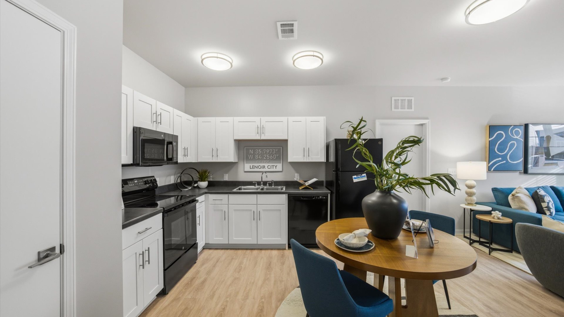 Modern kitchen with white cabinetry, gray counters, and black refrigerator beside a cozy dining nook.
